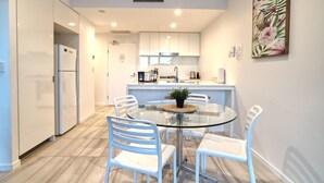 Une cuisine moderne avec des meubles blancs, une table à manger en verre et des chaises blanches.