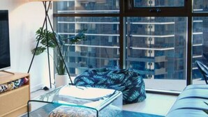 Un salon moderne avec une grande télévision, une table basse en verre, un fauteuil poire et un canapé.