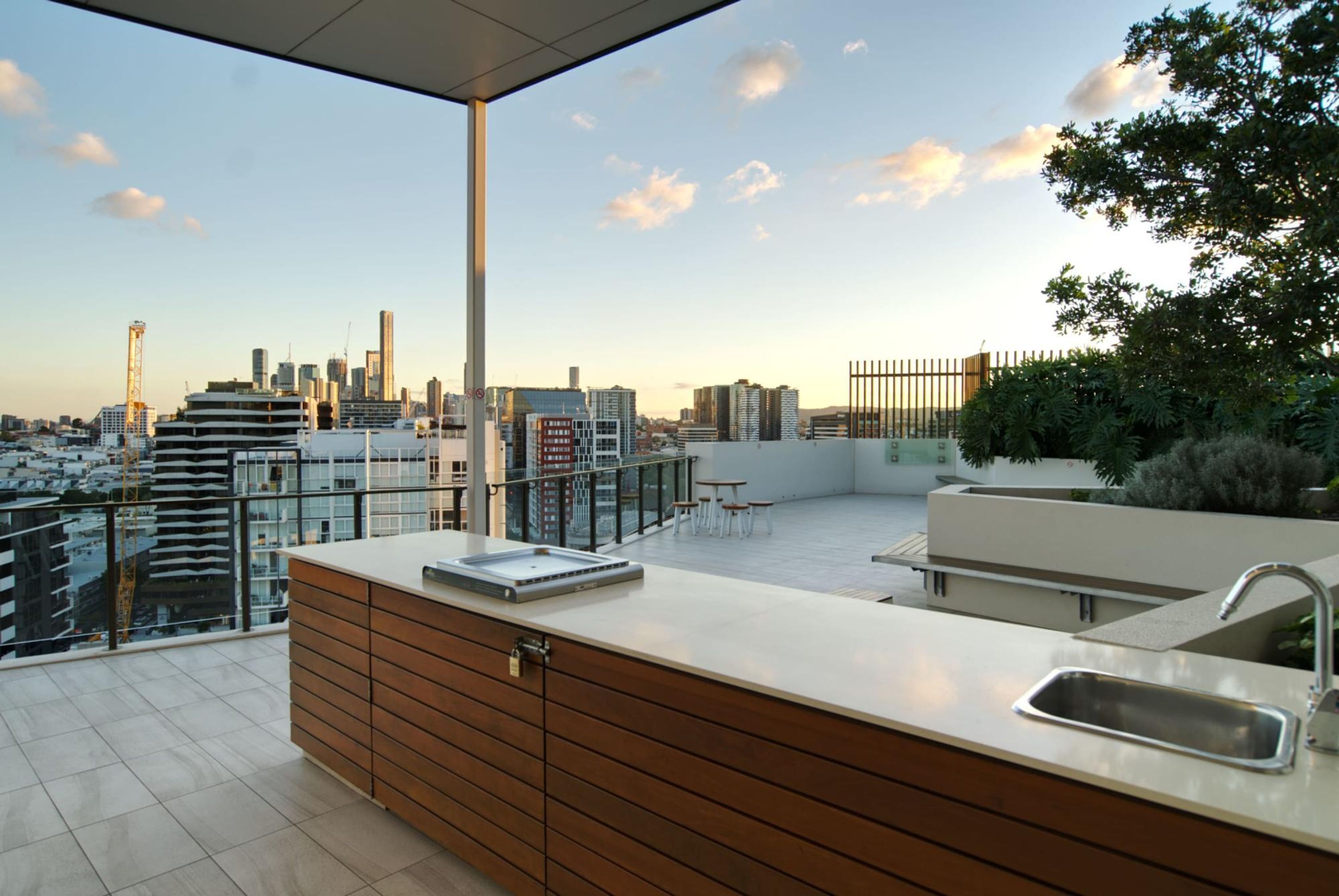 A modern rooftop terrace with a kitchen area, a city skyline view, and a glass railing.