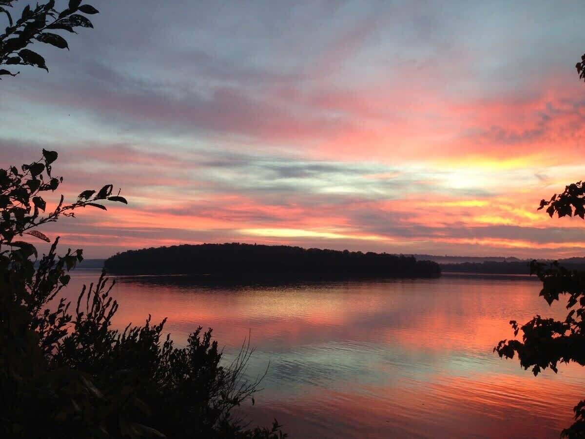 Un lac paisible au coucher du soleil, avec la silhouette d’une île qui se dessine à l’horizon.