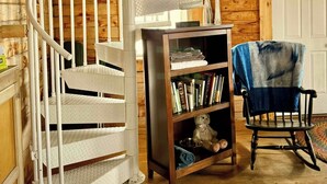 Een spiraaltrap in een houten chalet, met een boekenkast en een schommelstoel.