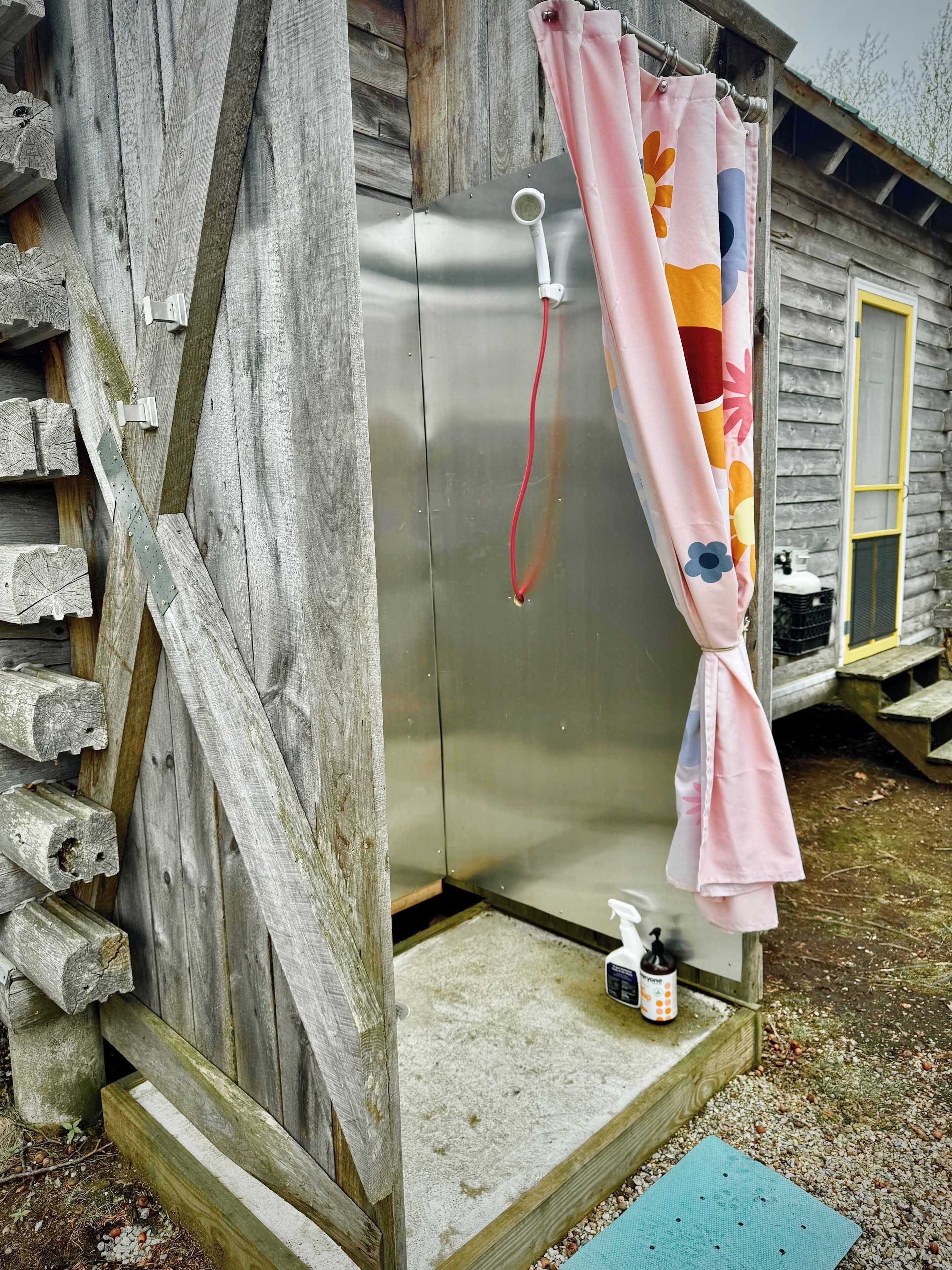 A rustic wooden cabin with a metal door, a pink shower curtain, and a small step leading to the entrance.