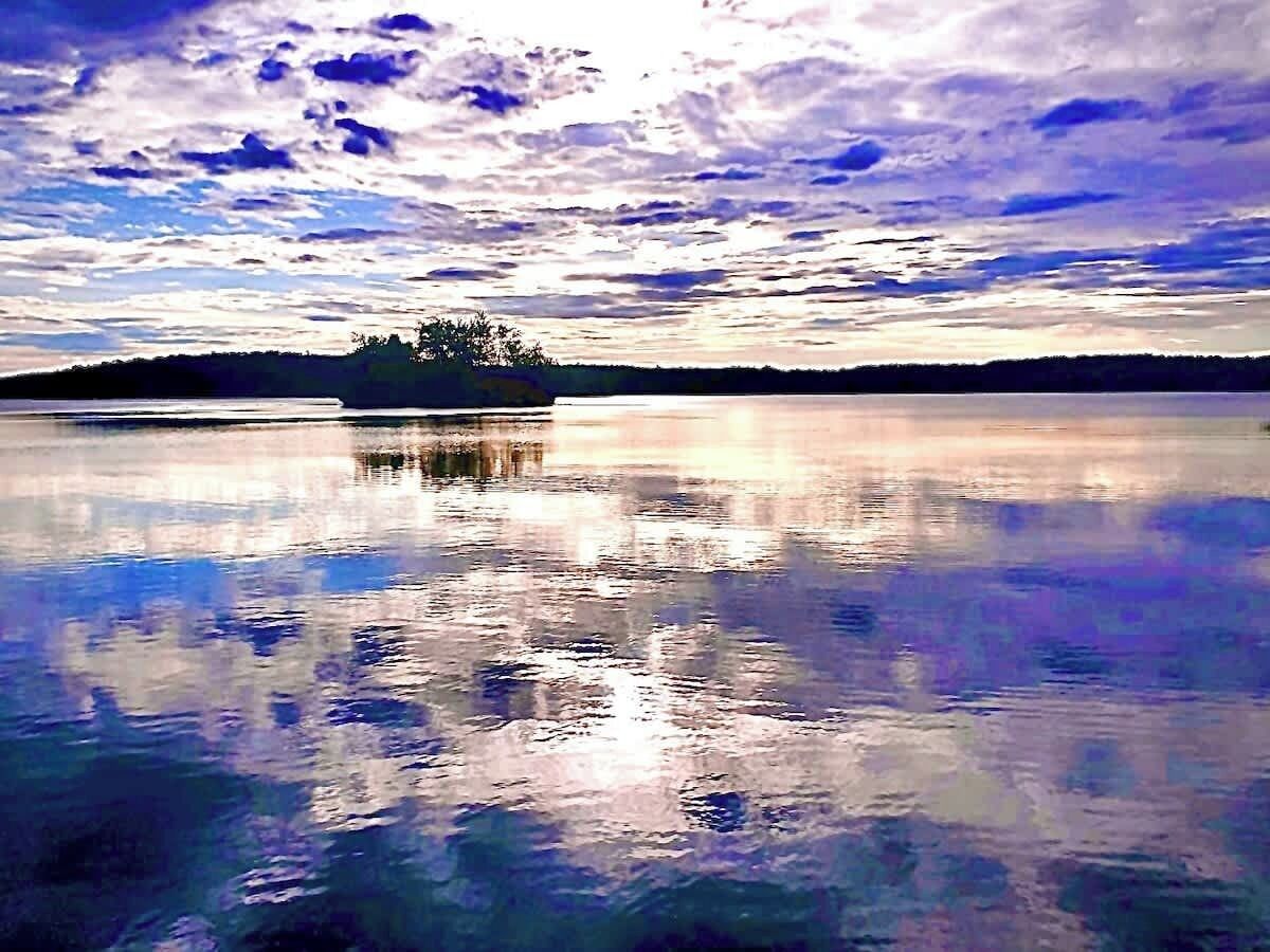 Ein ruhiger See mit einem klaren Spiegelbild des Himmels und einer kleinen Insel in der Ferne.
