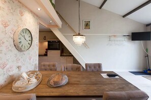 A dining area with a wooden table, cushioned chairs, a large wall clock, and a chandelier. - Nice vacation home in Horssen with garden (Horssen)