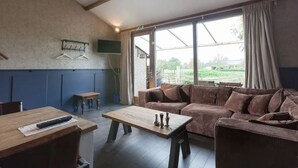 A cozy room with a large window, a sofa, a wooden table, and a TV mounted on the wall. - Nice vacation home in Horssen with garden (Horssen)