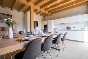 A modern dining area with a wooden ceiling, white cabinets, and a large table set for dining.