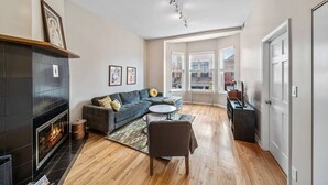 A modern living room with a fireplace, a sofa, a coffee table, and a view of the city through large windows. - Classic Lincoln Park  2 bedroom condo- parking included (Chicago)