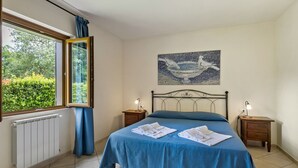 Una camera da letto con un letto, due comodini, una finestra, un termosifone e un quadro appeso al muro.