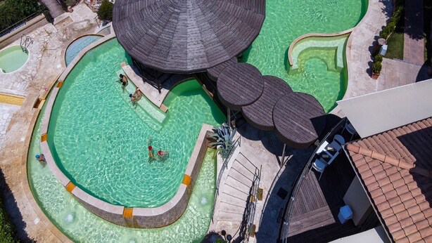 Una vista aerea di un resort con diverse piscine, una grande struttura a ombrello e un pontile in legno.