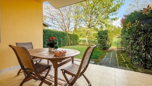 Un patio con una mesa y sillas de madera redonda, una planta en maceta y vistas de un jardín con un sendero y una verja.