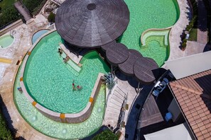 Vista aérea de um complexo de piscinas com várias atrações aquáticas, incluindo uma piscina central, uma piscina menor e uma área de hidromassagem.