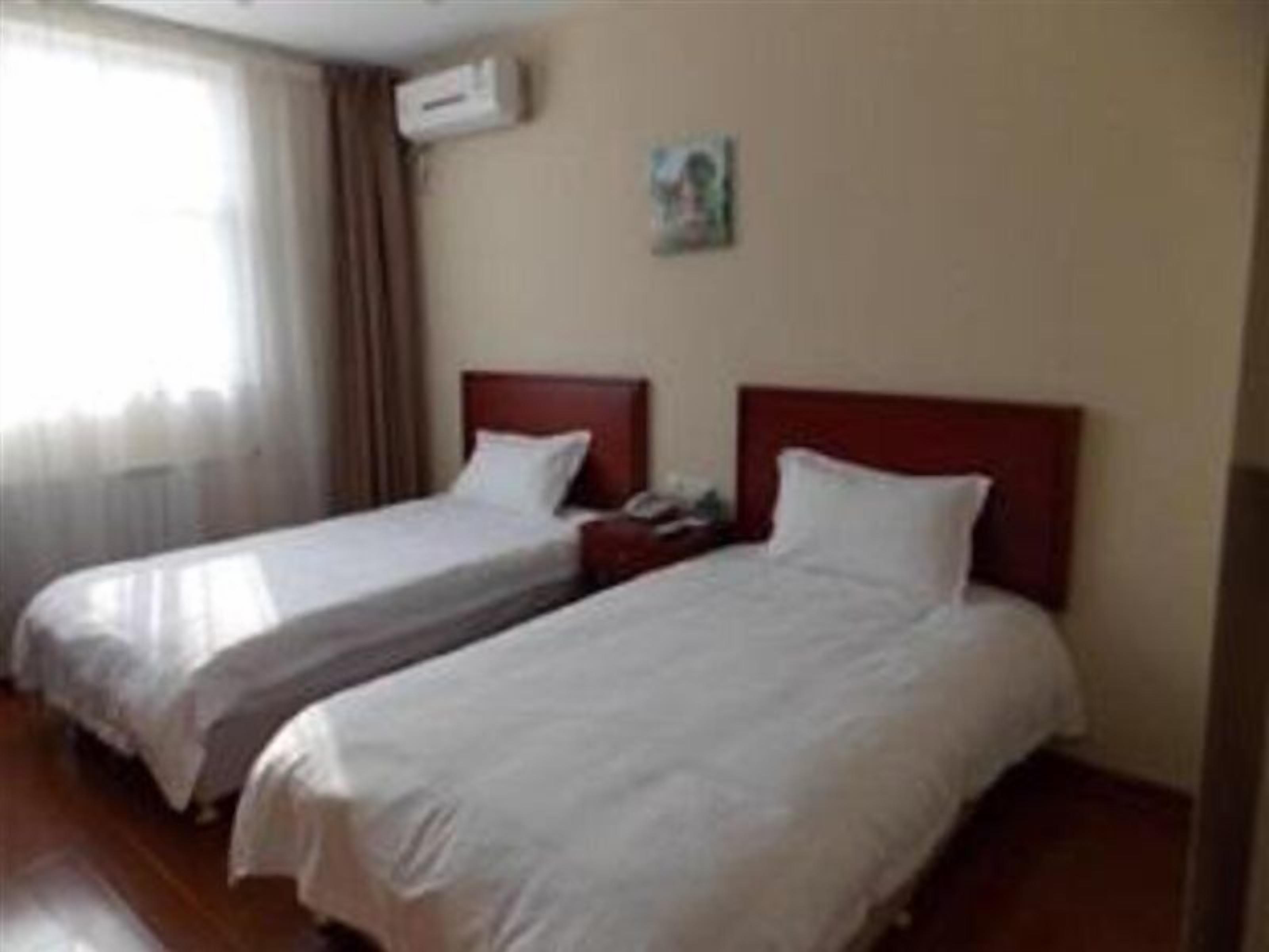 A hotel room with two single beds, a wooden floor, a window with curtains, and a wall-mounted air conditioner.