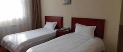 A hotel room with two single beds, a wooden floor, a window with curtains, and a wall-mounted air conditioner.