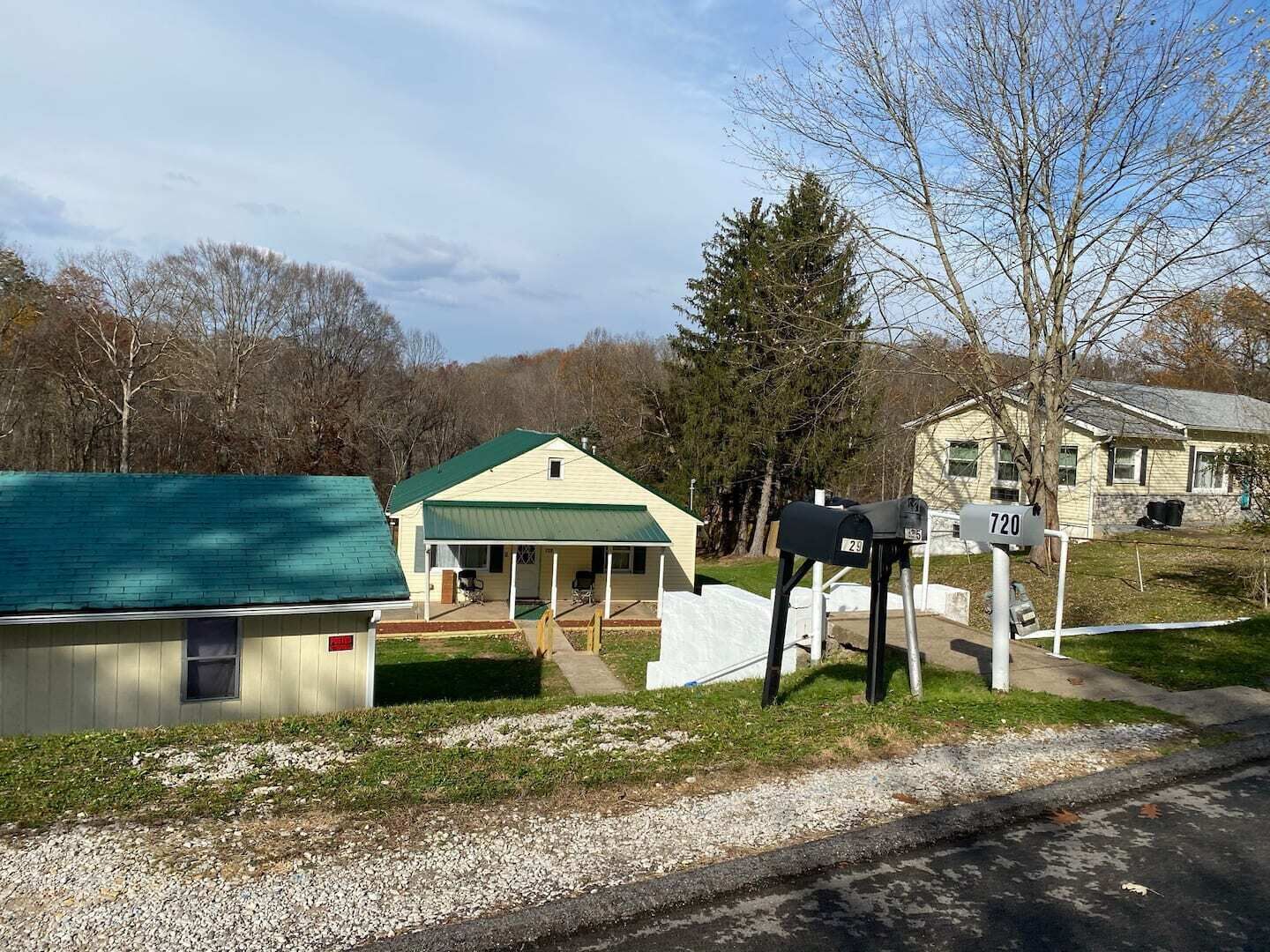 A small building with a green roof, a mailbox, and a house in the background.