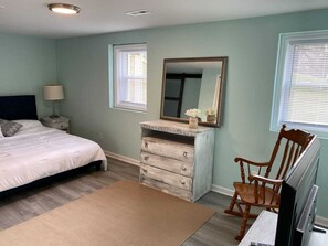 A bedroom with a bed, dresser, chair, and a television.