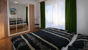 A bedroom with a bed, a mirror, a chair, and a window with green curtains. - Apartment in Scheffaui near Ski Slopes (Scheffau am Wilden Kaiser)