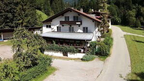 A two-story chalet with a balcony, surrounded by lush greenery and a mountain backdrop. - Apartment in Scheffaui near Ski Slopes (Scheffau am Wilden Kaiser)