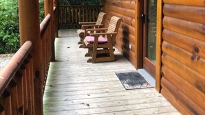 Une cabane en bois avec une véranda, deux chaises en bois et une porte.