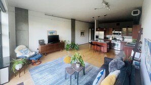 Un salon moderne avec un canapé, une table basse et un téléviseur posé sur un meuble en bois. On y trouve également un coin cuisine avec un bar et une table à manger.