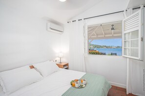 Une chambre avec un lit, une fenêtre donnant sur la mer, une table avec le petit-déjeuner et un appareil de climatisation.