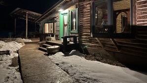 Puinen mökki, jossa on kuisti, penkki ja lumipeitteinen maa.