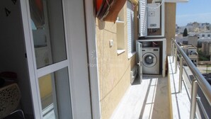 Ein schmaler Balkon mit Waschmaschine, Wäschekorb und einem Technikschrank.