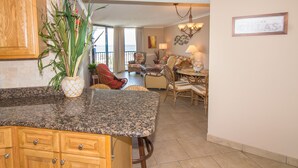 A kitchen with granite countertops, wooden cabinets, and a dining area with wicker chairs and a chandelier.