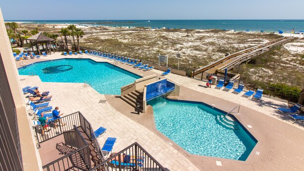 A pool area with two swimming pools, sun loungers, and a view of the beach.