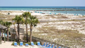 A beach view with lounge chairs, palm trees, and a rocky shoreline.