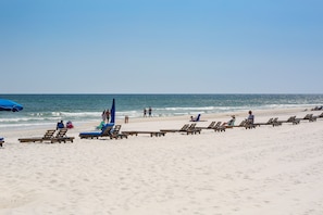 A beach with rows of wooden lounge chairs and a blue umbrella. - SUN ~SAND ~MAKE MEMORIES! ~BEAUTIFUL DIRECT BEACHFRONT ~SUANA ~RESORT AMENITIES! (Orange Beach)