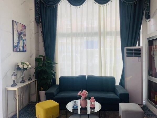 A living room with a dark blue sofa, a yellow ottoman, a white coffee table, and a potted plant. - Shell Shanghai Songjiang District Xinqiao Town Xinqiao Hotel (Shanghai)