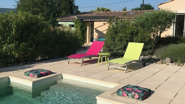 A swimming pool with two lounge chairs and a small table, surrounded by greenery and a building with a tiled roof. - House with swimming pool in lavender fields near the Gorges du Verdon (Bras-d'Asse)