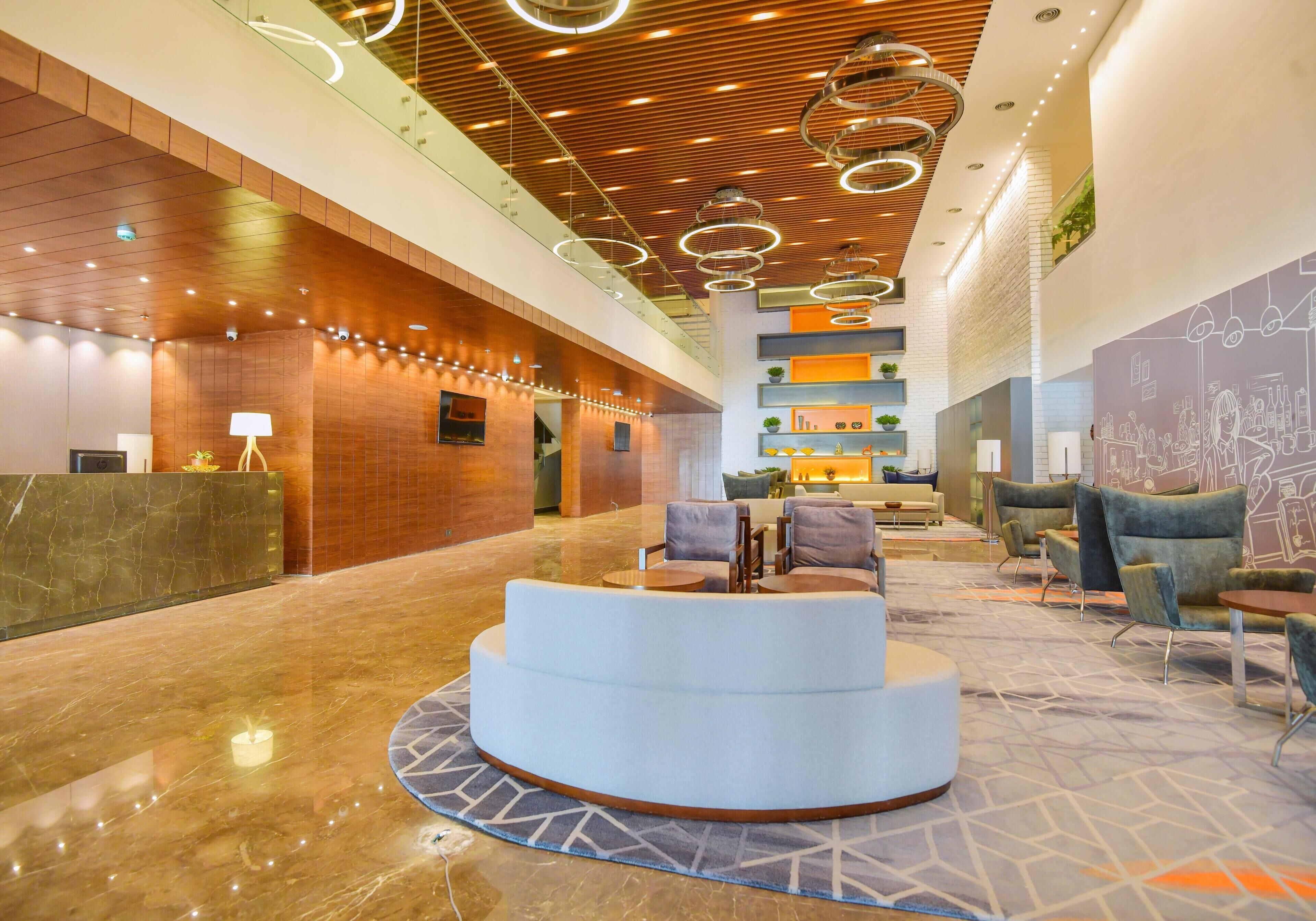 A hotel lobby with a reception desk, seating area, and a staircase.