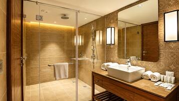 A modern bathroom with a glass-enclosed shower, a large mirror, and a vanity with toiletries.