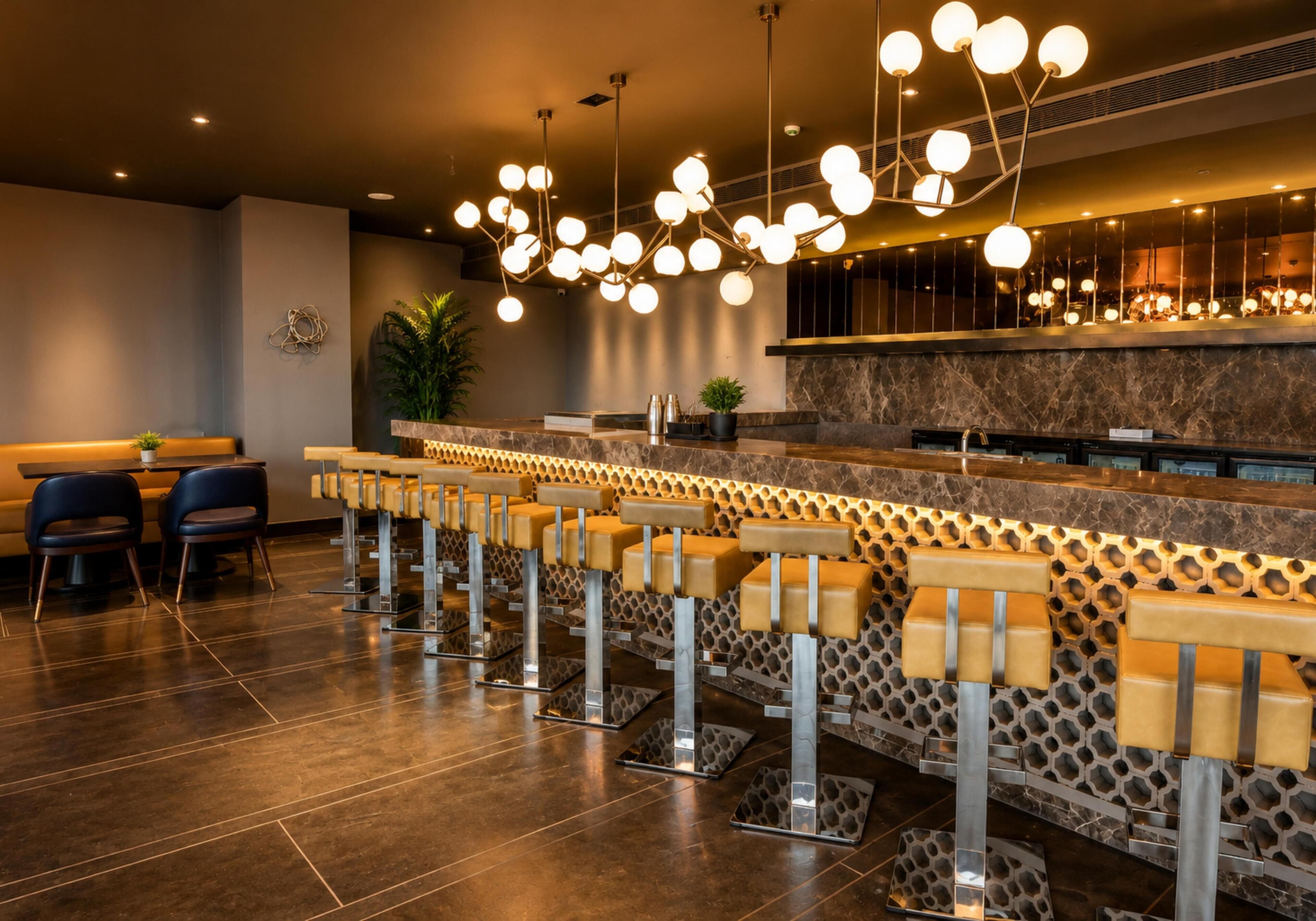 A modern bar area with a long counter, multiple seating options, and a unique ceiling light fixture.