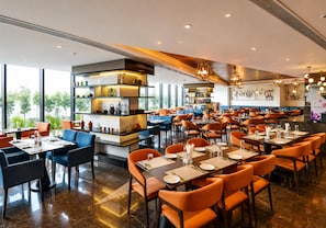 A modern restaurant with a variety of seating options, including tables and booths, and a bar area with shelves displaying decorative items. - The Elite Narasapura, a member of Radisson Individuals (Kolar)