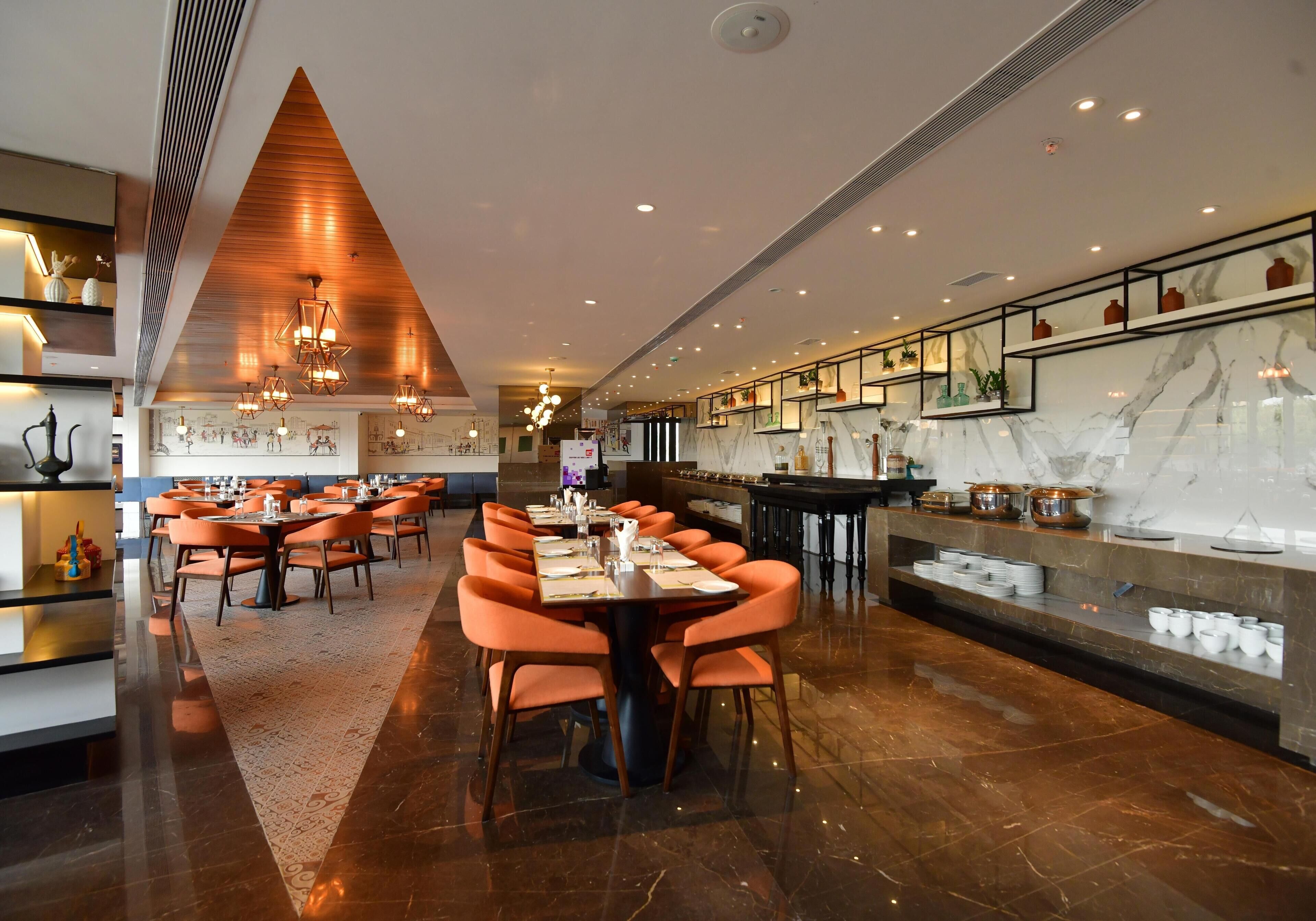 Un restaurante moderno con un amplio comedor, múltiples mesas y una barra de mármol.