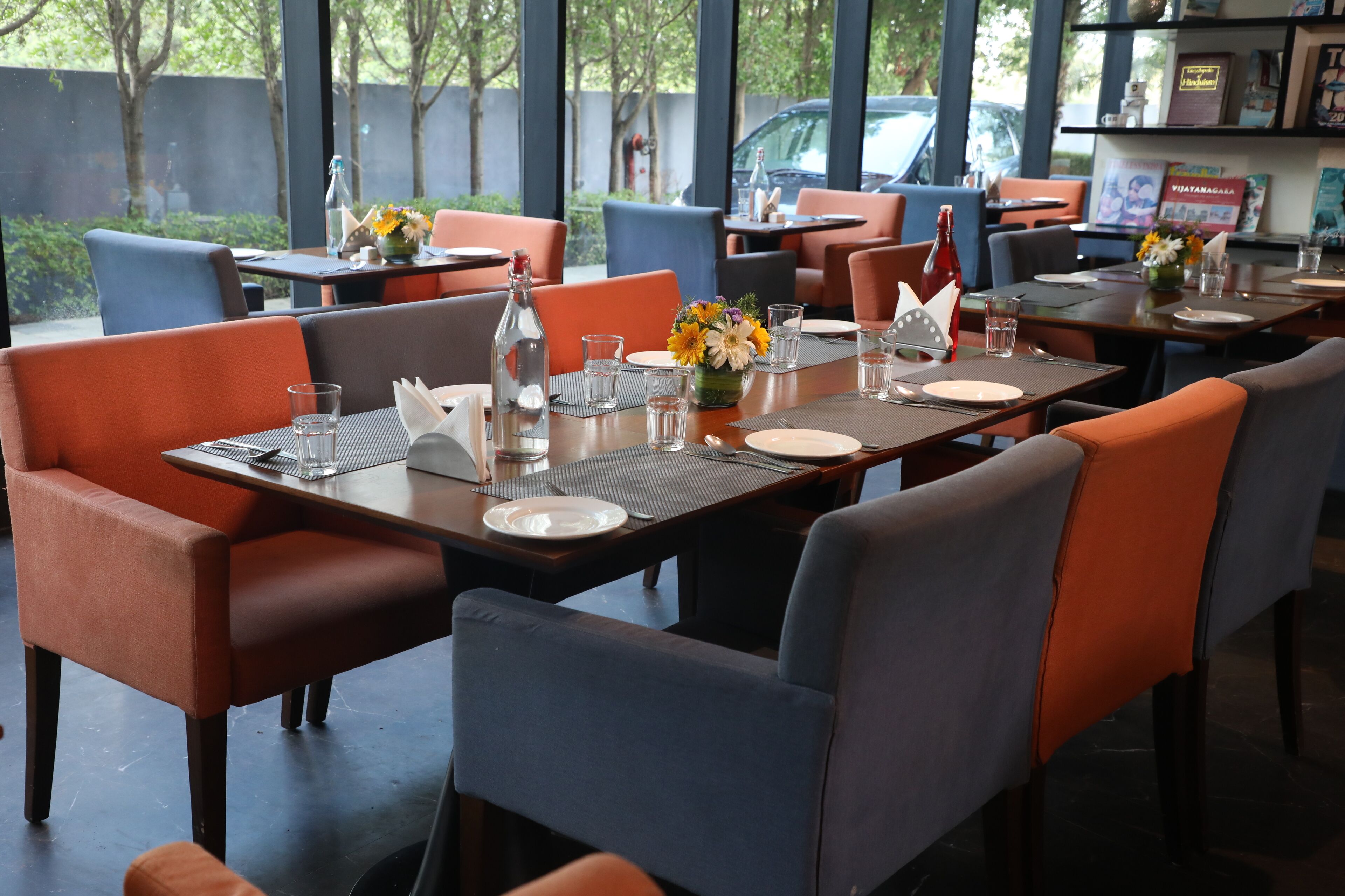 Een restaurant met gedekte tafels, met oranje en blauwe stoelen, en uitzicht op de omgeving.