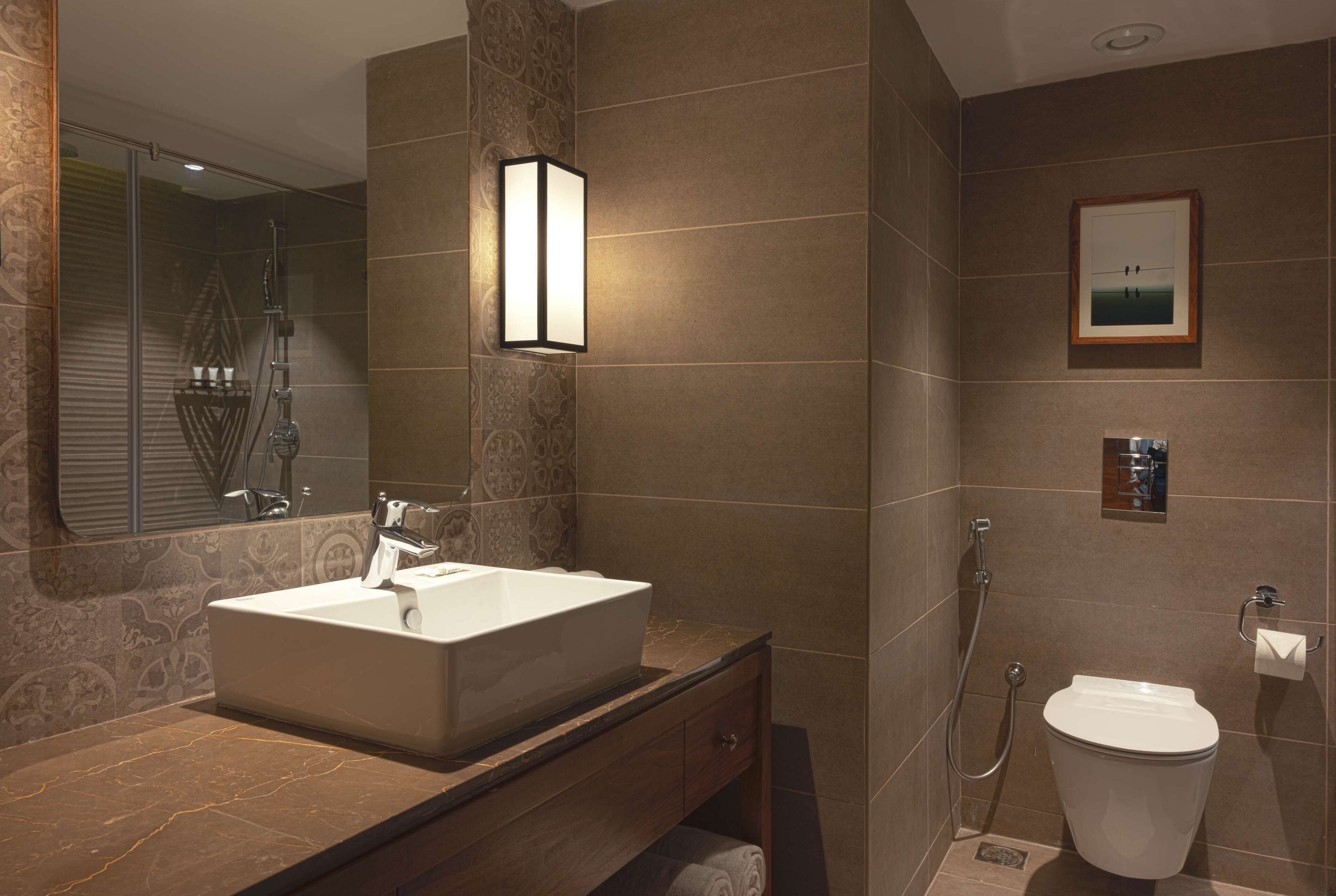 A modern bathroom with a large sink, a shower, and a toilet.