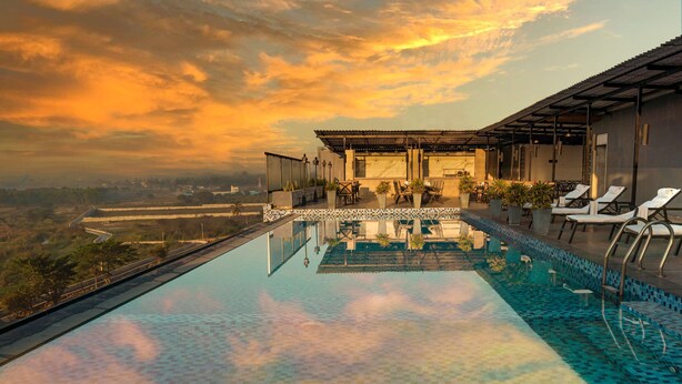 A rooftop infinity pool with a view of the landscape, a bar area, and lounge chairs.
