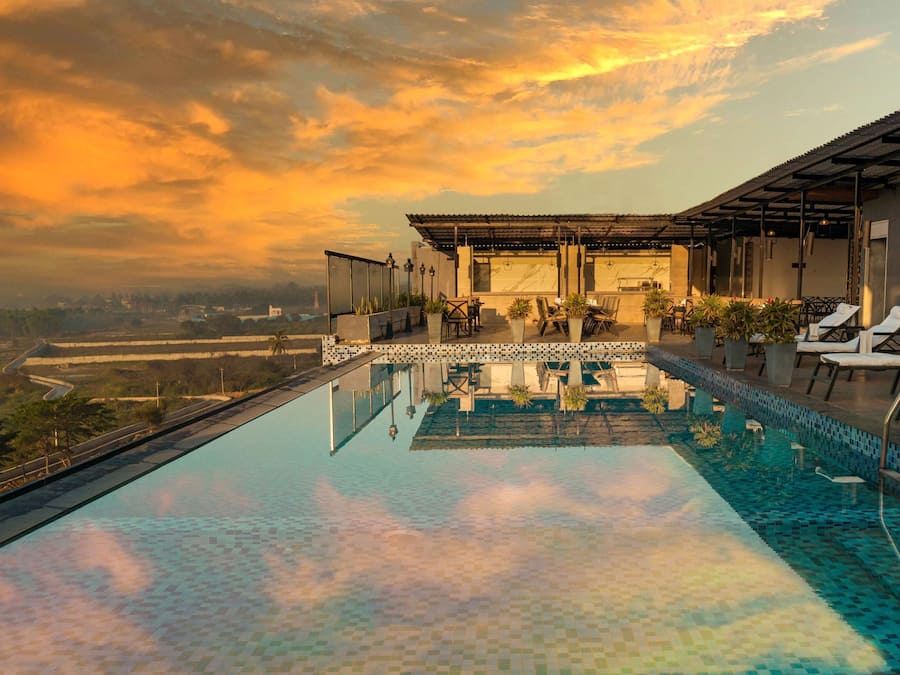 A rooftop infinity pool with a view of the landscape, a bar area, and lounge chairs.