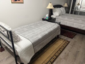 A room with two single beds, a nightstand with a lamp, a mirror, and a patterned rug. - Two Bedroom Basement only home near UGA - with newly renovated floors!! (Athens)