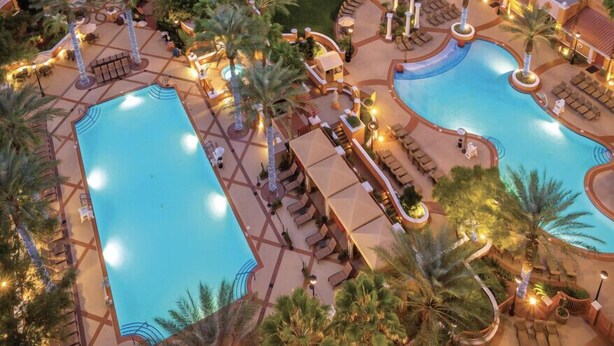 Un hôtel doté de plusieurs piscines, de palmiers et d’espaces de détente en plein air.