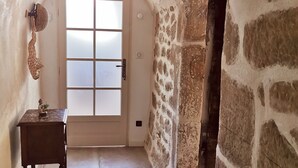 A narrow hallway with a stone wall, a wooden table with a statue, and a frosted glass door. - Cottage in a charming house (Vernoux-en-Vivarais)
