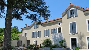 A two-story building with a symmetrical facade, multiple windows with shutters, and a gravel courtyard with a table and chairs. - Cottage in a charming house (Vernoux-en-Vivarais)