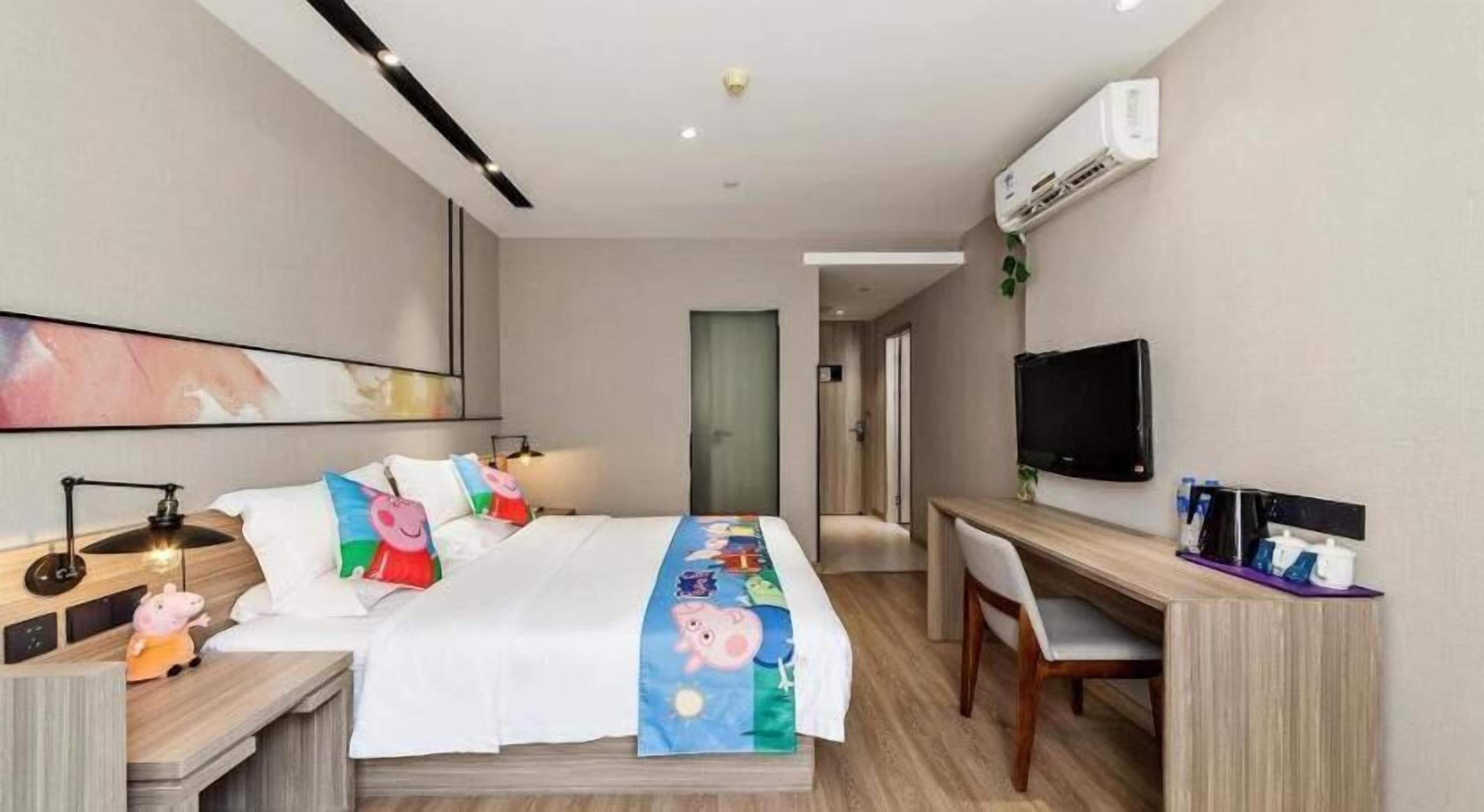 Ein Hotelzimmer mit Bett, Nachttisch, Lampe, Fernseher, Schreibtisch, Stuhl und Klimaanlage.