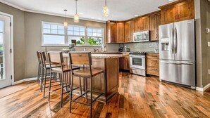 Une cuisine moderne avec des meubles en bois, des appareils en acier inoxydable et un îlot central doté de tabourets de bar.