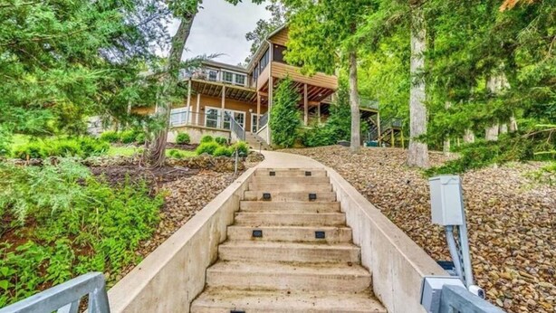 Un escalier menant à une maison en bois dotée d’un balcon, le tout entouré d’une végétation luxuriante.