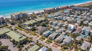 Vue aérienne d’un quartier résidentiel situé sur la côte, avec une plage, comprenant des immeubles à plusieurs étages et des maisons individuelles, et une zone de piscine est indiquée par un cercle.