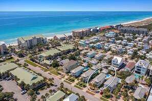 Vista aerea di una zona residenziale costiera con spiaggia, che include edifici a più piani e case unifamiliari, con un'area piscina evidenziata.